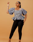 Model wearing blue and gold Ankara peplum top with puff sleeves and fitted black pants.