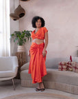 Woman wearing an orange satin crop top and matching ruched skirt, styled with statement glasses
