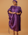 Woman wearing a regal purple satin kaftan with side drawstring detail and matching head wrap.
