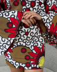 Woman wearing a bold Ankara two-piece set with flared sleeves and a fitted skirt in red, yellow, and black floral prints.