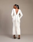 Woman wearing the Zola white maxi dress with bateau neckline, rhinestone embellishments, long sleeves, deep V-back plunge, and hemline slit.