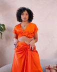 Woman wearing an orange satin crop top and matching ruched skirt, styled with statement glasses