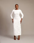 Woman wearing the Zola white maxi dress with bateau neckline, rhinestone embellishments, long sleeves, deep V-back plunge, and hemline slit.