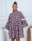 Model wearing a short flared Ankara dress with white lace sleeve detailing in a minimalist living room setting.
