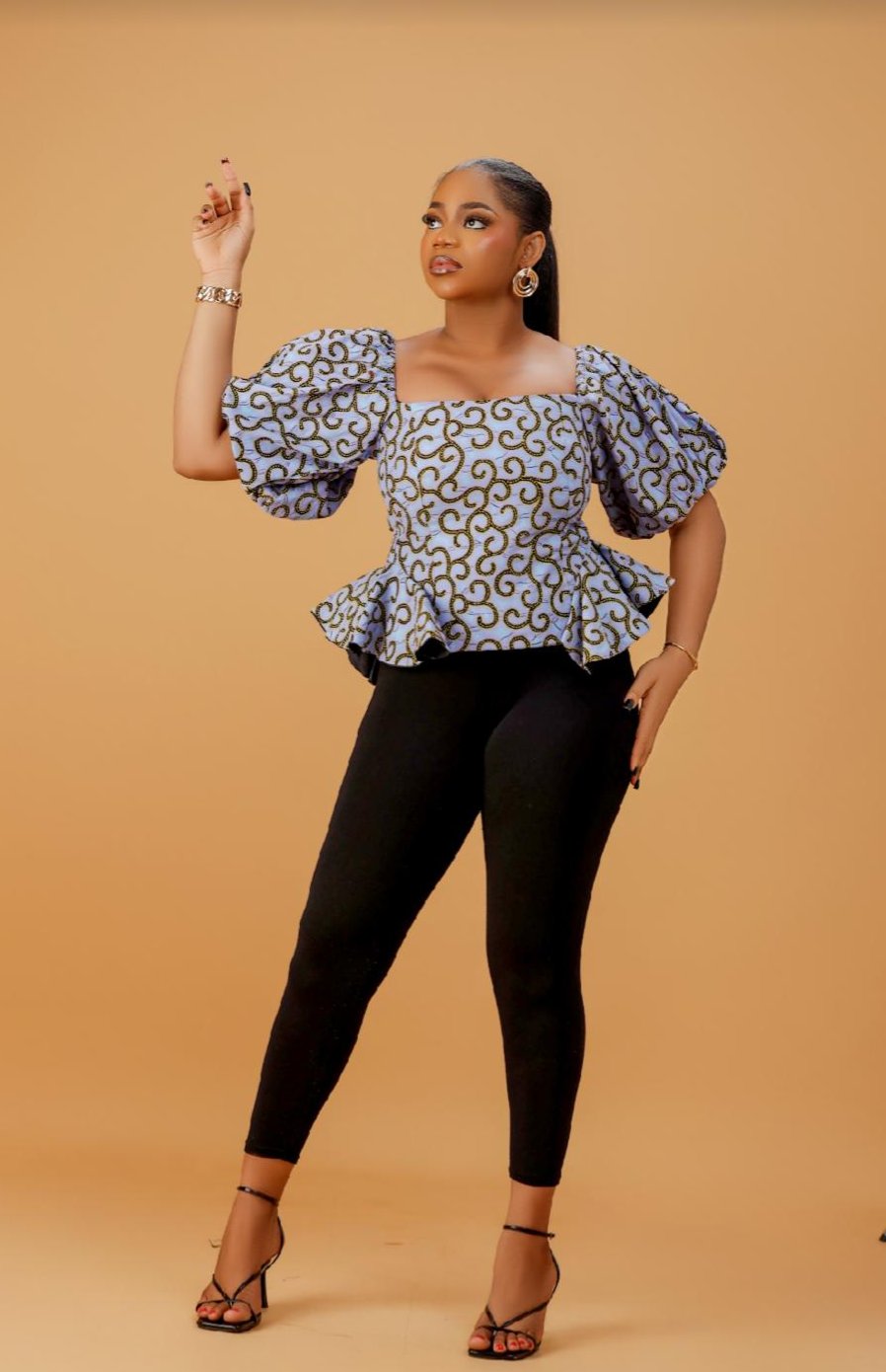 Model wearing blue and gold Ankara peplum top with puff sleeves and fitted black pants.
