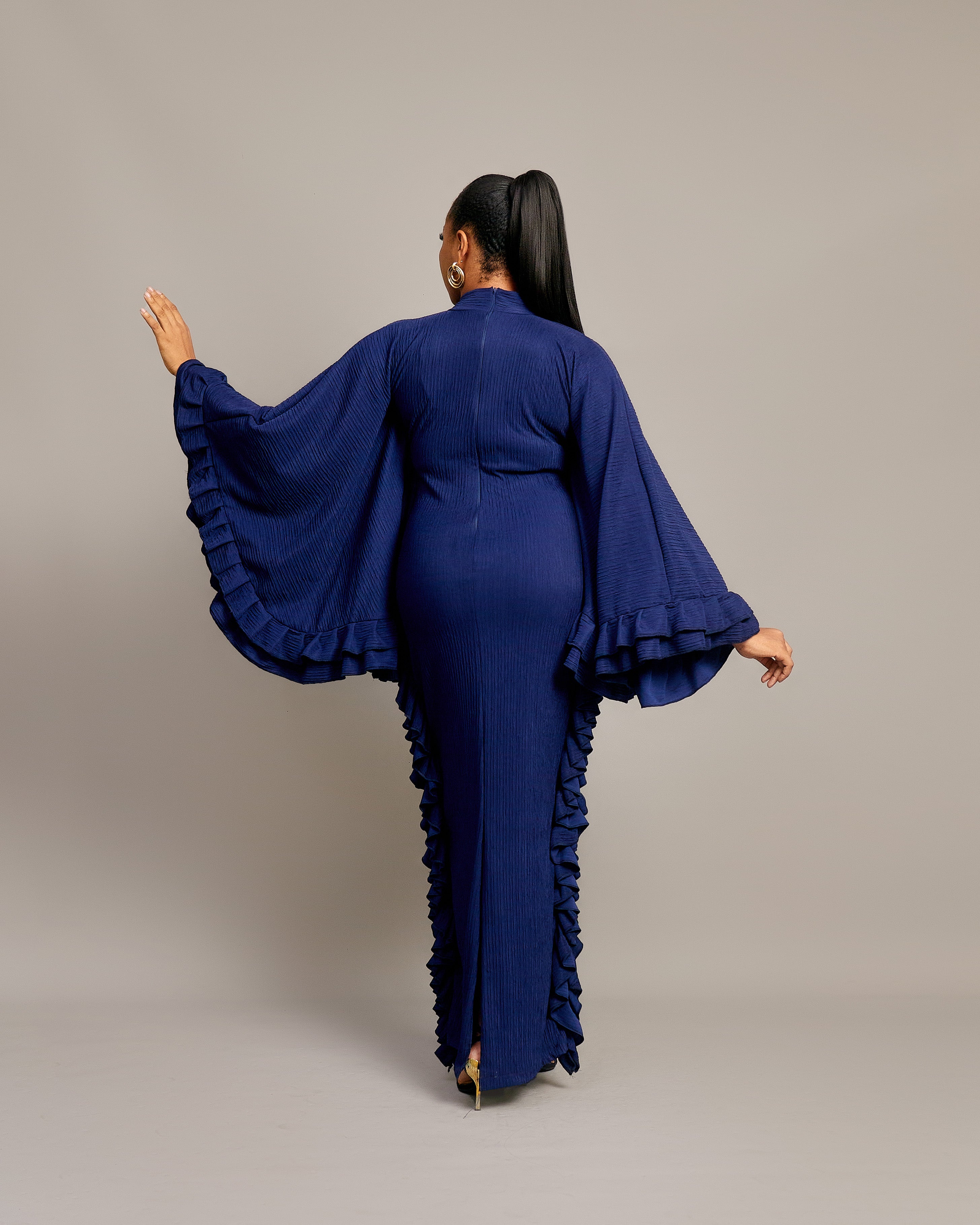 woman wearing the Tella Dress: one in ivory, one in navy. Maxi gowns with ruffle sides, long sleeves, and bow-tie neckline.
