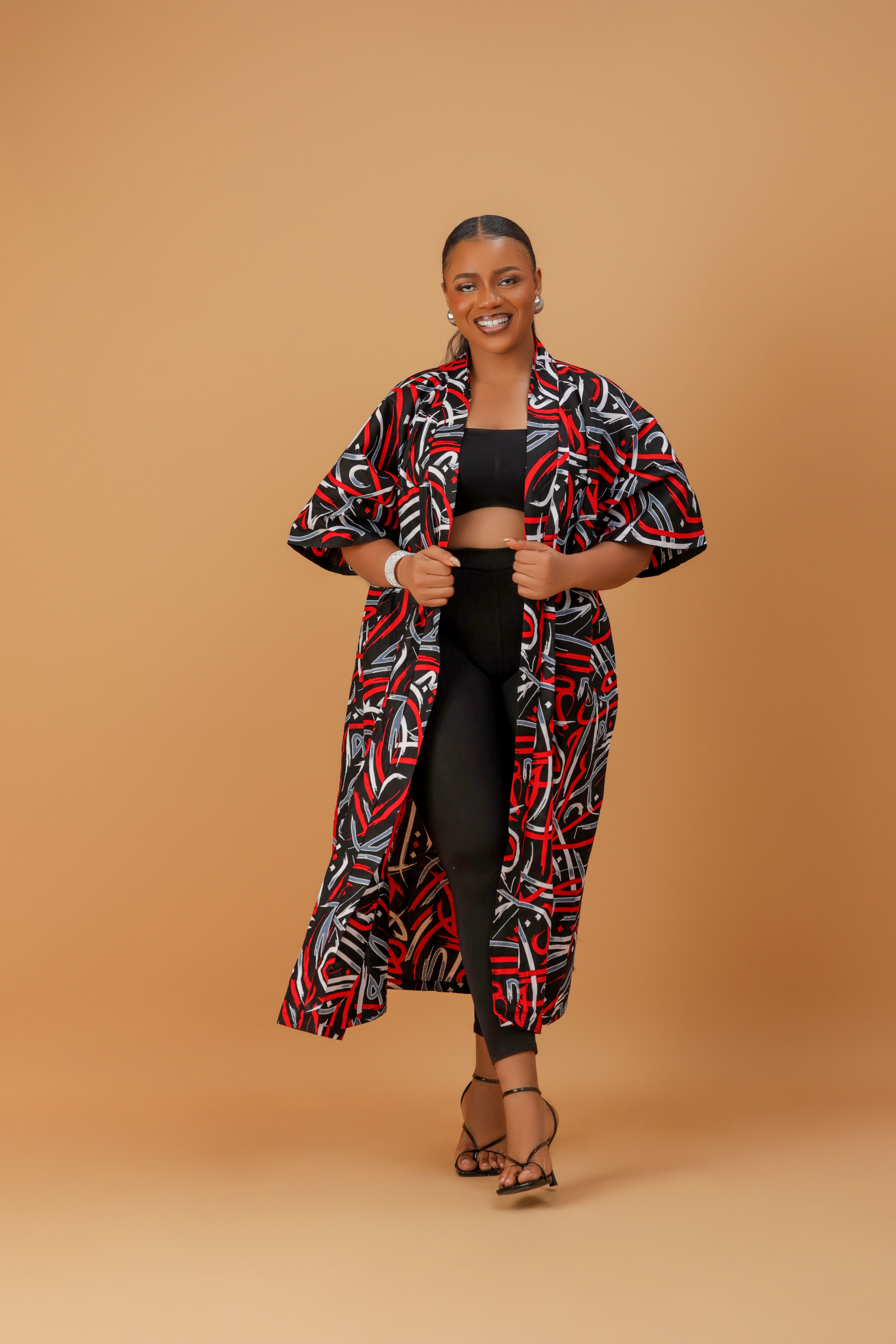 Woman wearing a bold red, black, and white abstract print kimono over a black crop top and leggings.
