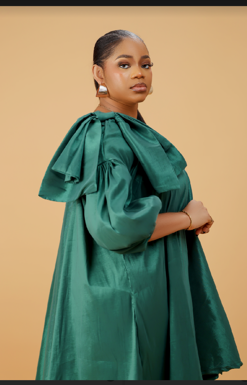 Model wearing an emerald green satin bow sleeve dress with voluminous sleeves and structured bow detail on the shoulder.
