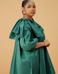 Model wearing an emerald green satin bow sleeve dress with voluminous sleeves and structured bow detail on the shoulder.
