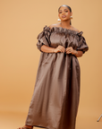 Woman wearing an off-shoulder brown maxi dress with puff sleeves and a flowing ankle-length design on a neutral background.
