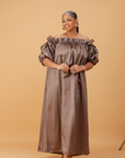 Woman wearing an off-shoulder brown maxi dress with puff sleeves and a flowing ankle-length design on a neutral background.

