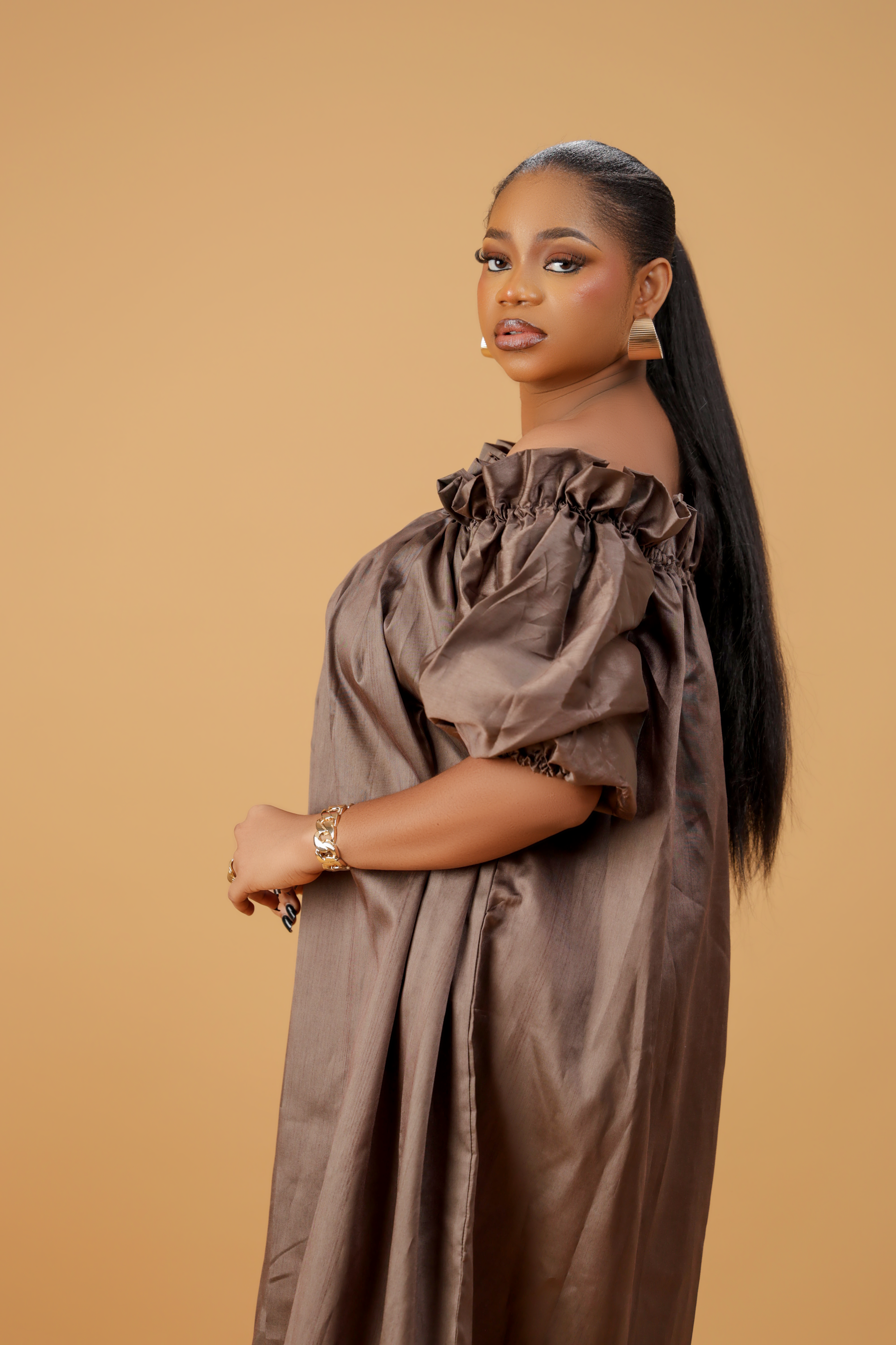 A woman wearing a brown off-shoulder maxi dress with puffed sleeves.