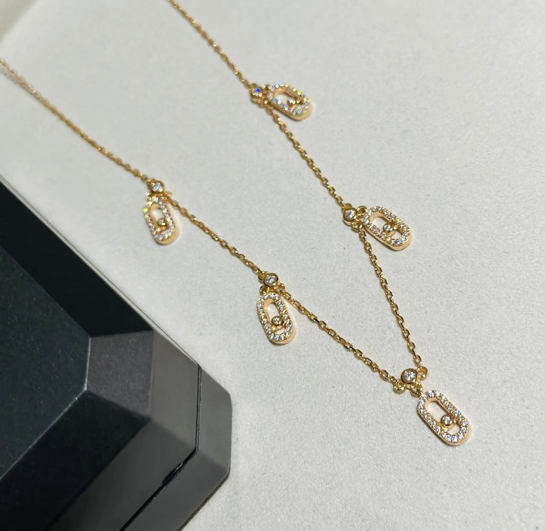 Gold chain necklace with crystal-studded oval pendants displayed in a black jewelry box.
