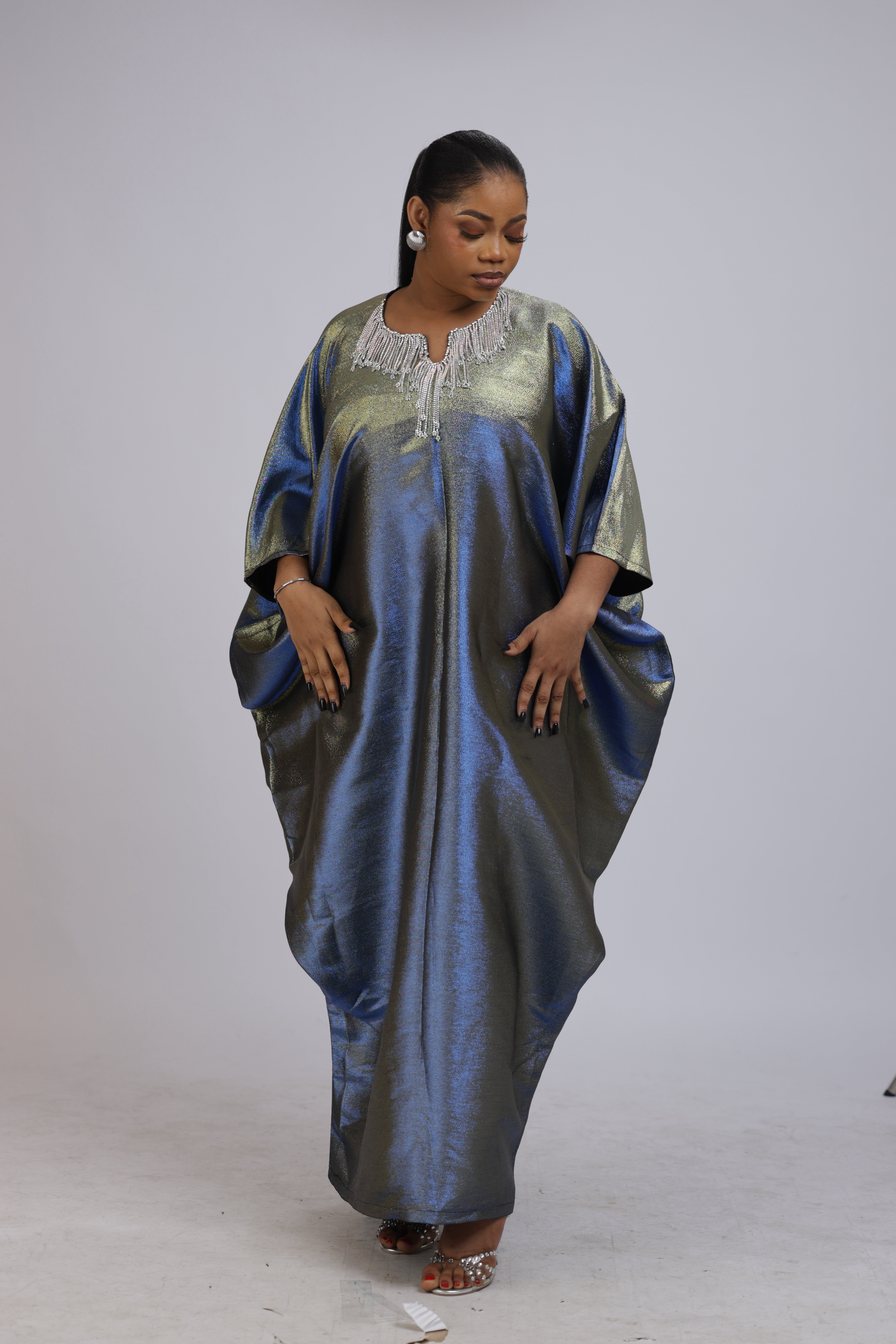 Woman wearing a shiny metallic blue-green cupped chain dress with loose sleeves and embellished neckline.
