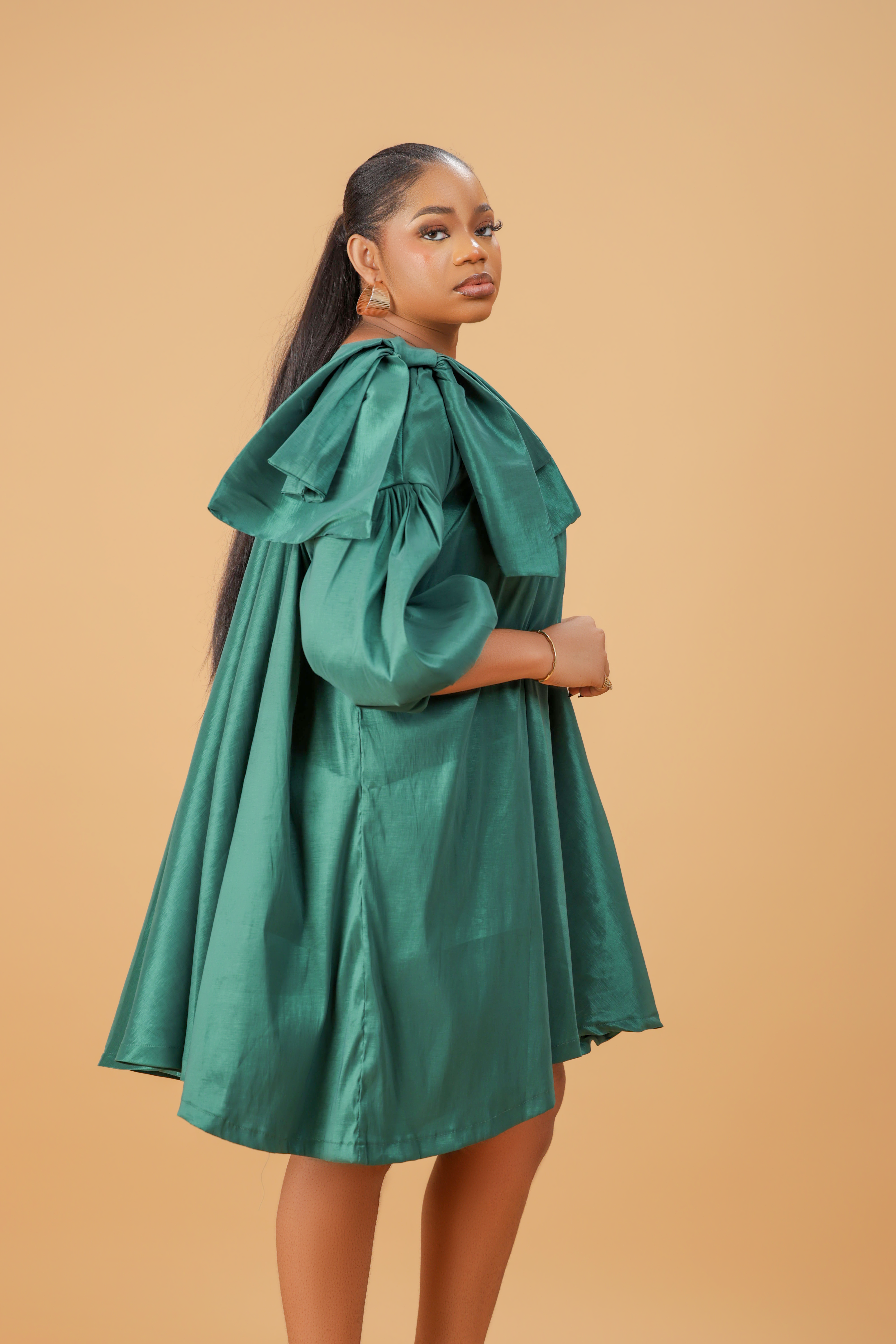 Model wearing an emerald green satin bow sleeve dress with voluminous sleeves and structured bow detail on the shoulder.
