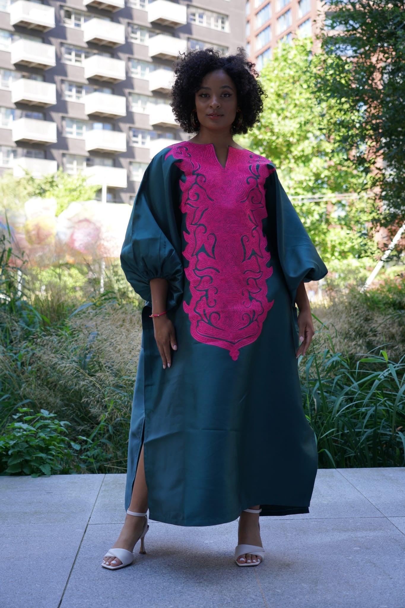 Model wearing luxurious teal Boubou dress with bold pink embroidery and voluminous sleeves.
