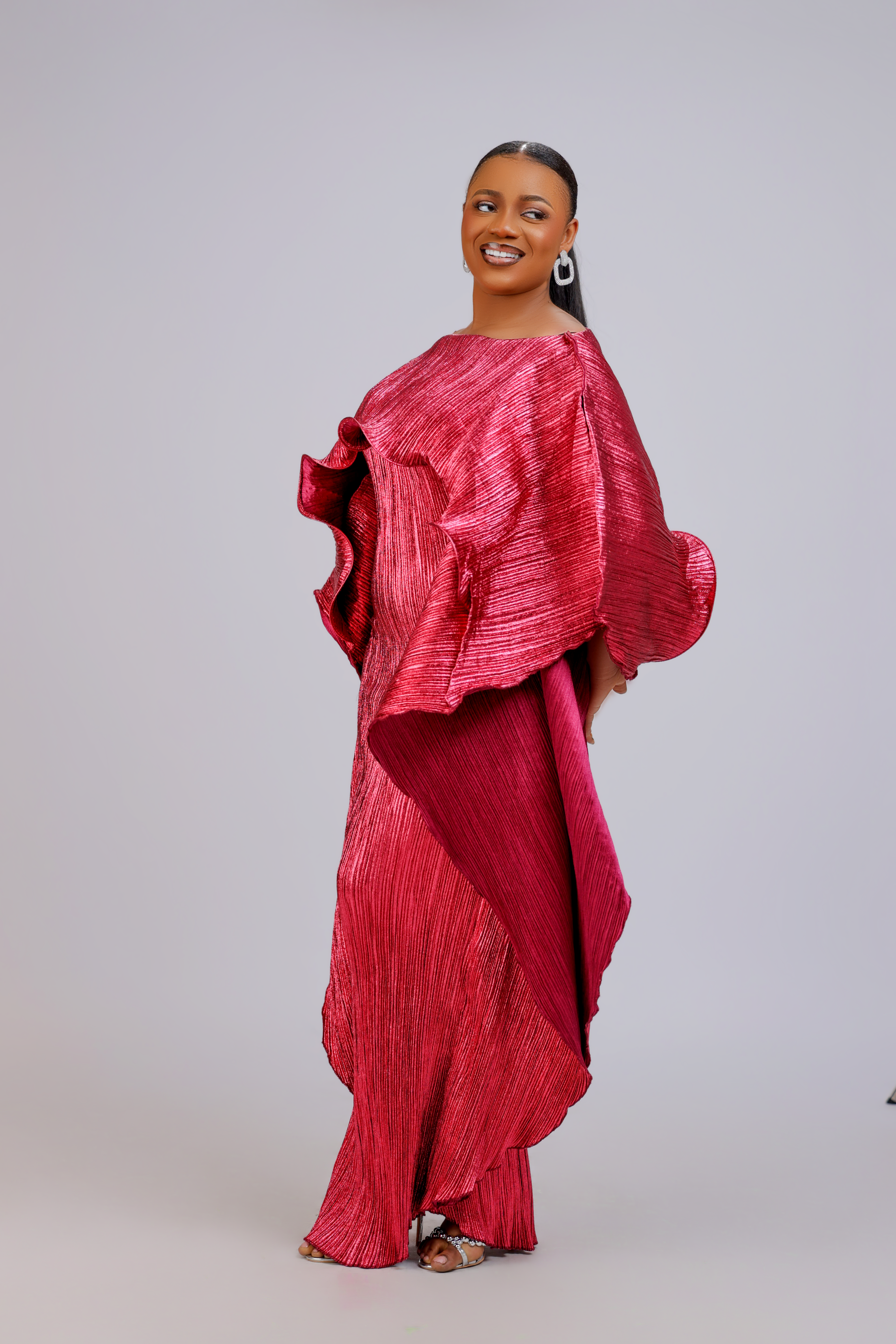 Woman wearing an elegant fuchsia pleated gown with ruffle detailing and asymmetrical layers.
