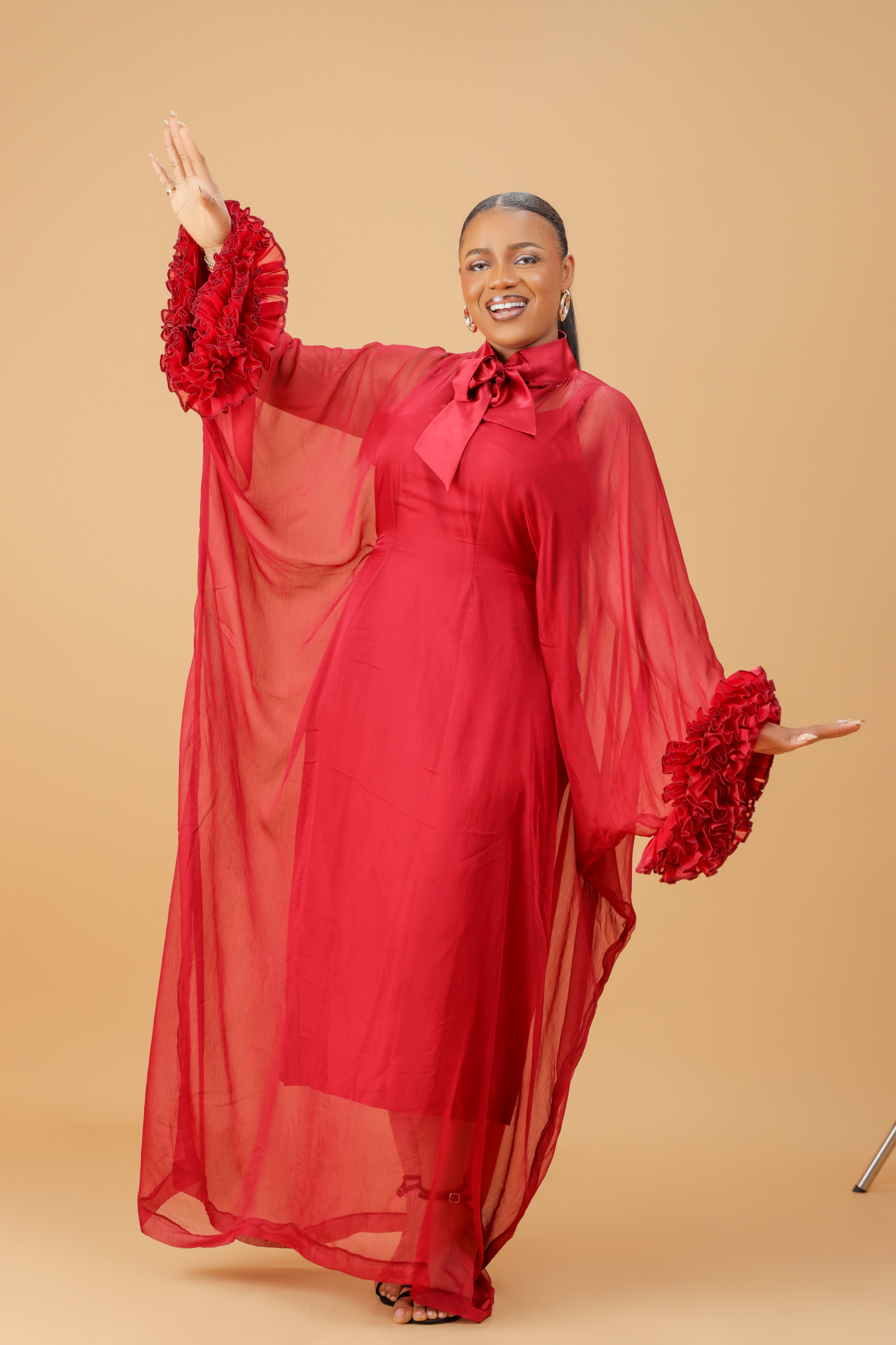 Model wearing a red organza statement dress with bow-tie neck and textured floral sleeve details, styled for formal and festive occasions.
