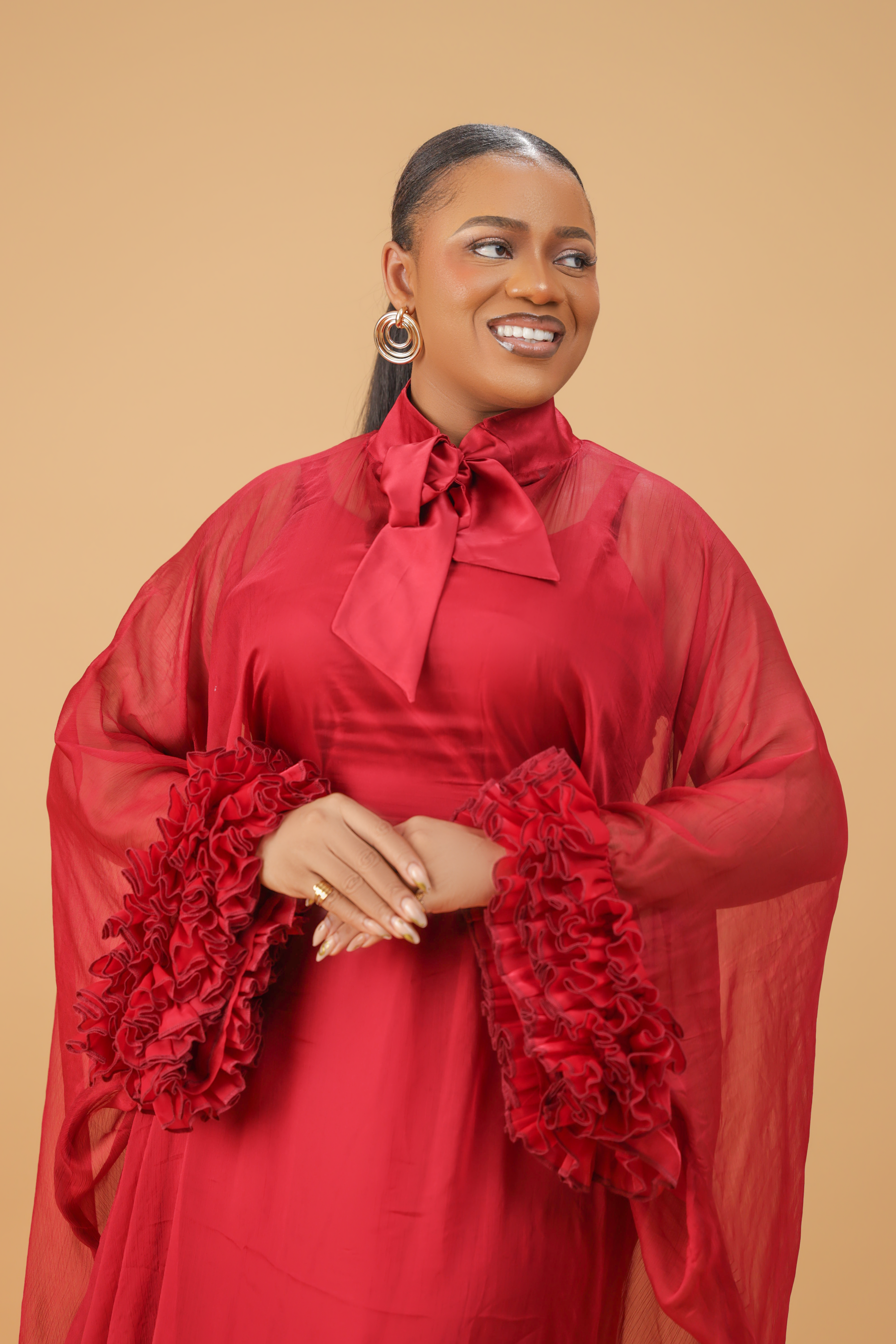 Model wearing a red organza statement dress with bow-tie neck and textured floral sleeve details, styled for formal and festive occasions.
