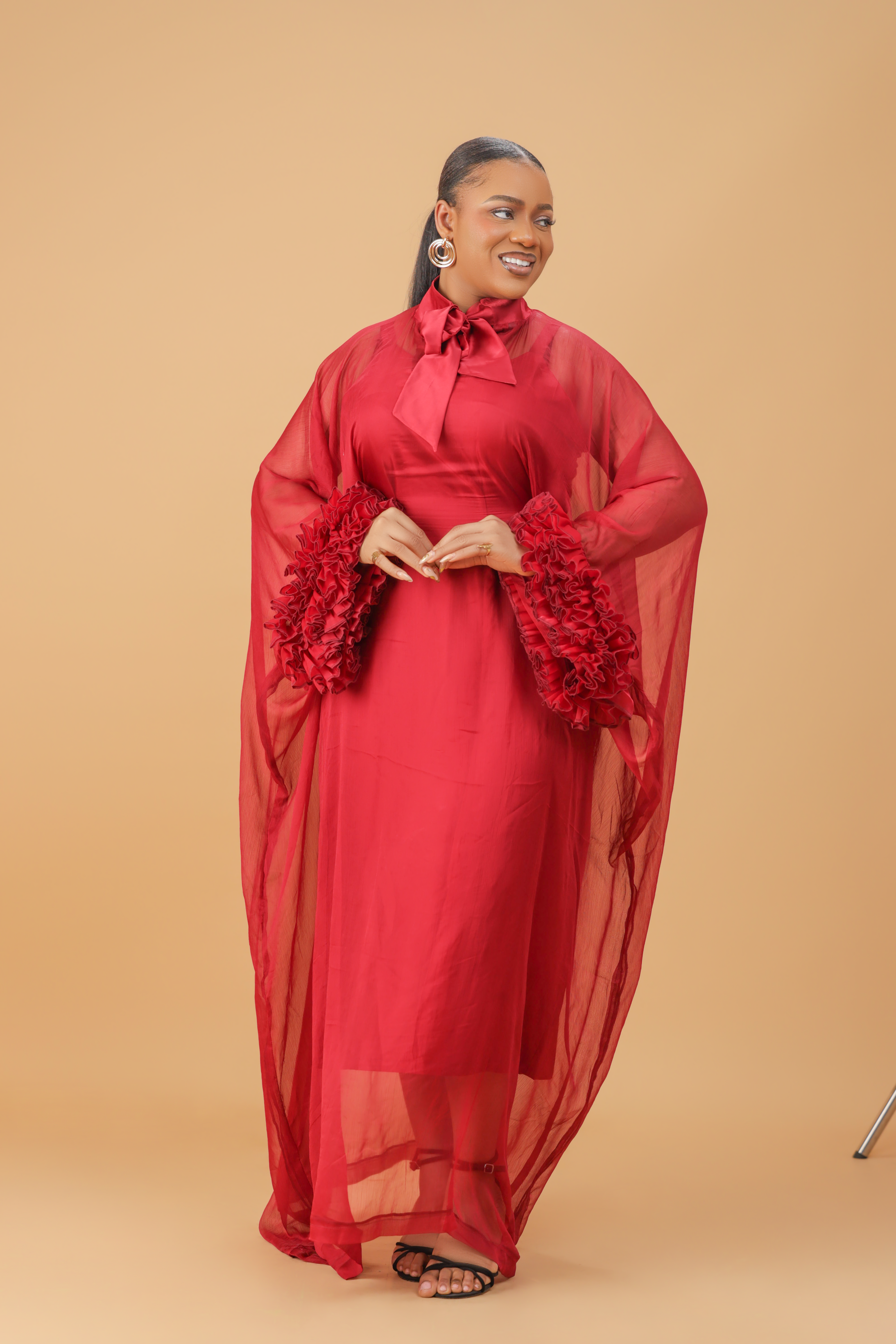Model wearing a red organza statement dress with bow-tie neck and textured floral sleeve details, styled for formal and festive occasions.
