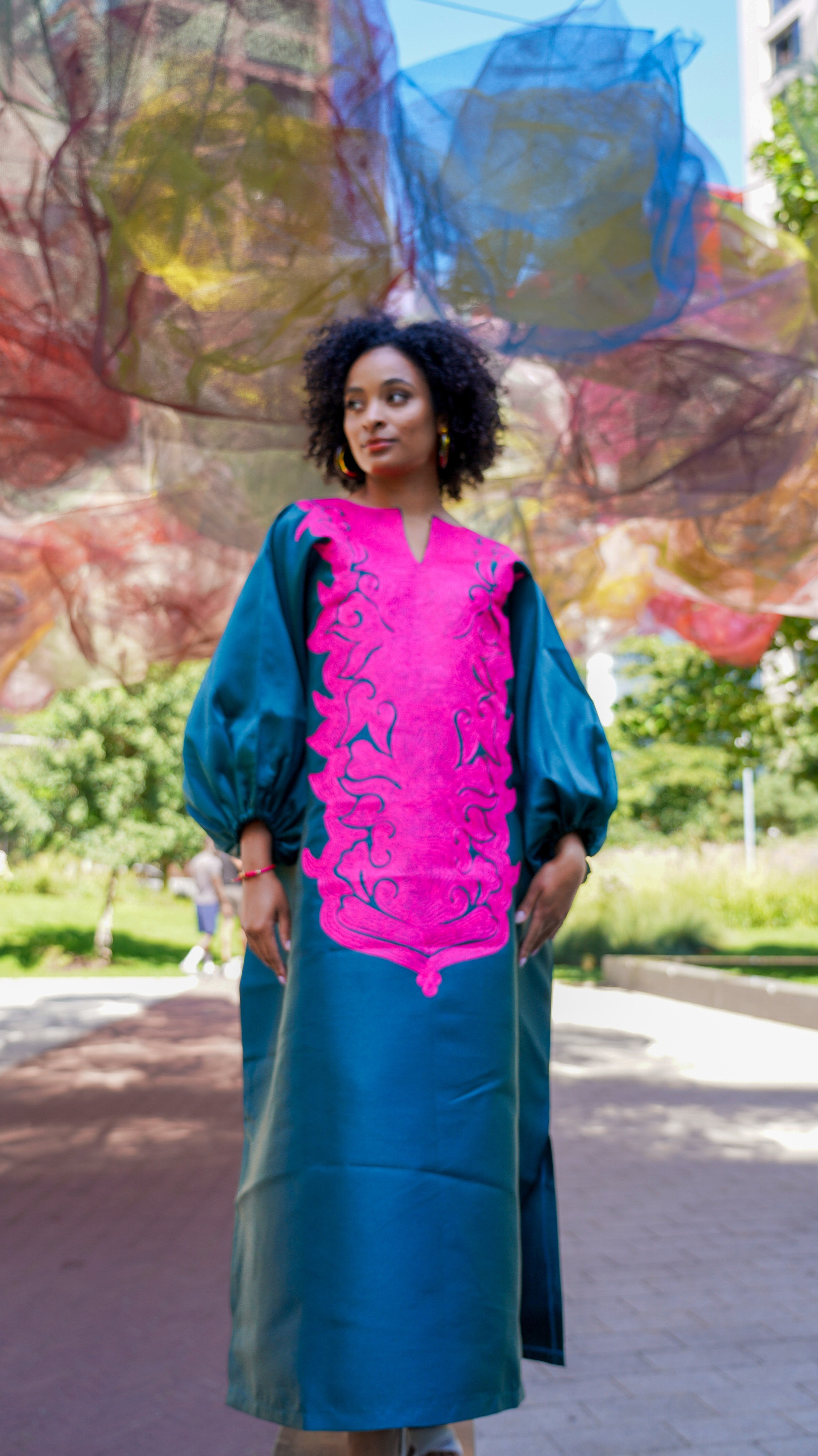 Model wearing luxurious teal Boubou dress with bold pink embroidery and voluminous sleeves.
