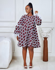 Model wearing a short flared Ankara dress with white lace sleeve detailing in a minimalist living room setting.
