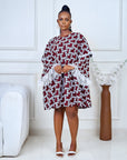 Model wearing a short flared Ankara dress with white lace sleeve detailing in a minimalist living room setting.

