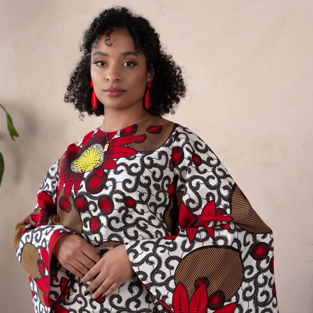 Woman wearing a bold Ankara two-piece set with flared sleeves and a fitted skirt in red, yellow, and black floral prints.
