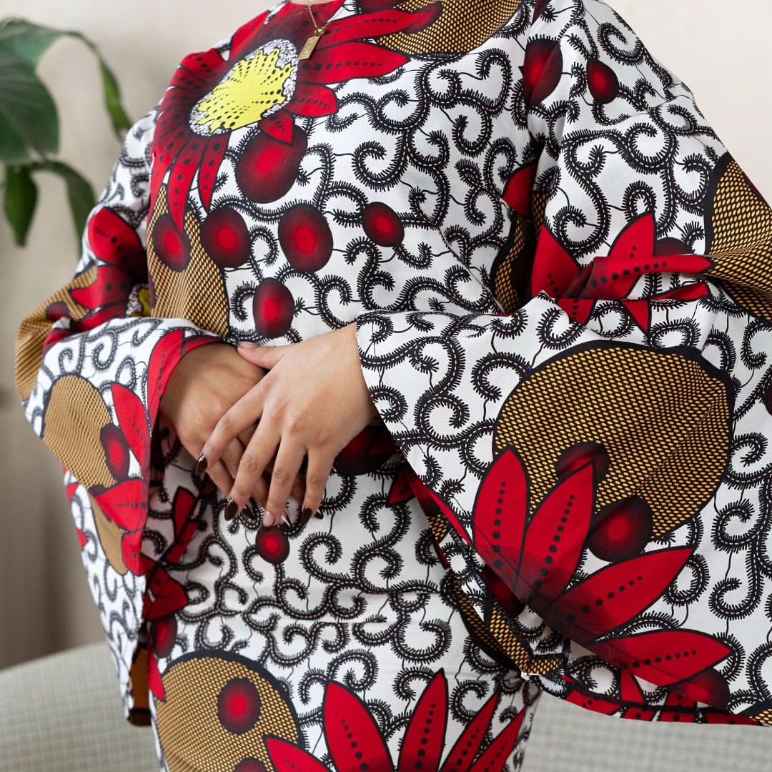 Woman wearing a bold Ankara two-piece set with flared sleeves and a fitted skirt in red, yellow, and black floral prints.
