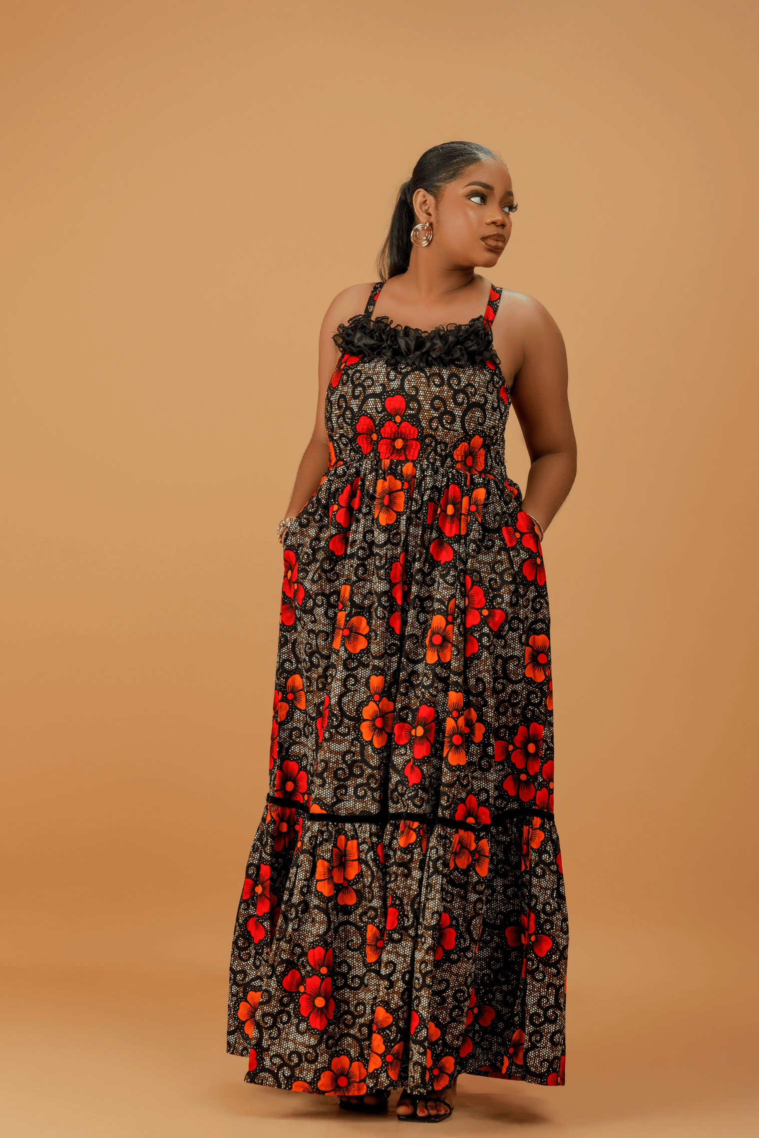 Model wearing a sleeveless cotton maxi dress with bold red and orange floral print, smocked bodice, and tiered skirt.
