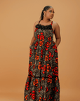 Model wearing a sleeveless cotton maxi dress with bold red and orange floral print, smocked bodice, and tiered skirt.