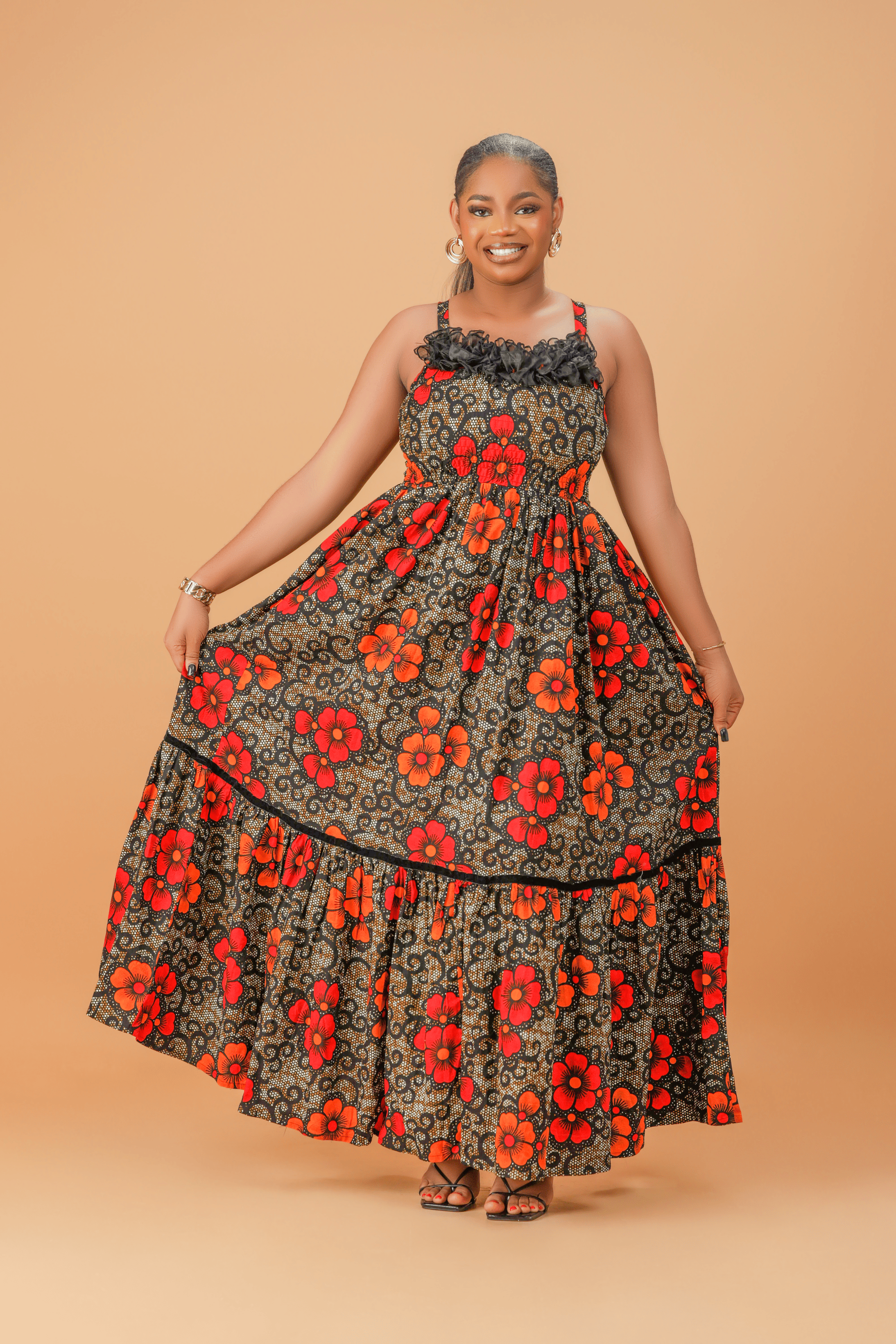 Model wearing a sleeveless cotton maxi dress with bold red and orange floral print, smocked bodice, and tiered skirt.