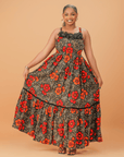 Model wearing a sleeveless cotton maxi dress with bold red and orange floral print, smocked bodice, and tiered skirt.