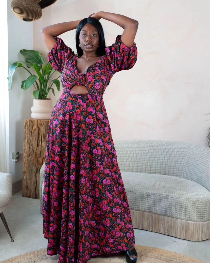 Woman wearing a long floral cut-out dress with puff sleeves in red and purple tones.
