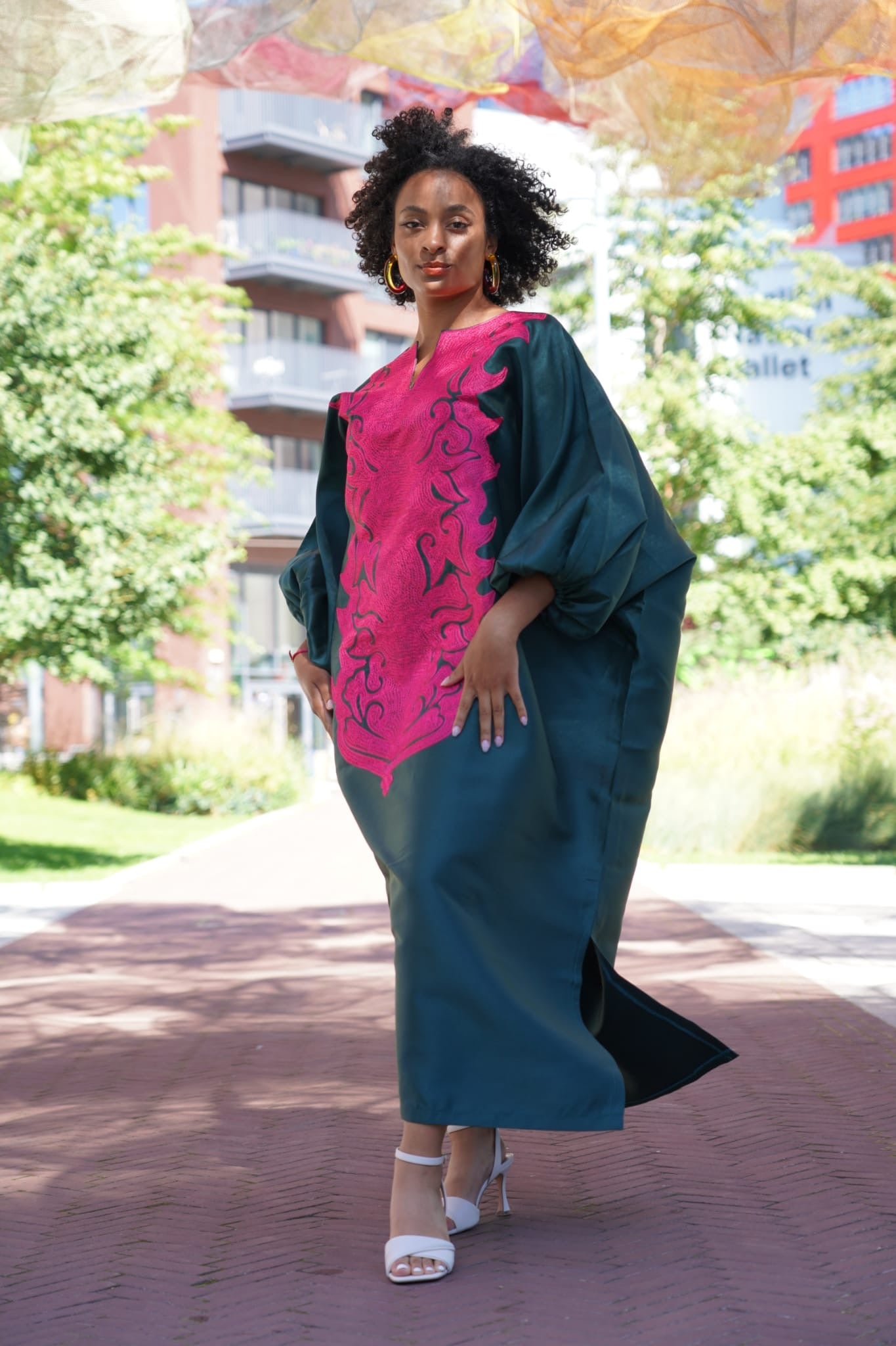 Model wearing luxurious teal Boubou dress with bold pink embroidery and voluminous sleeves.
