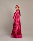 Woman wearing the Ola Buubu satin gown in pink with ruffle edges, long sleeves, high neckline, and matching headwrap.
