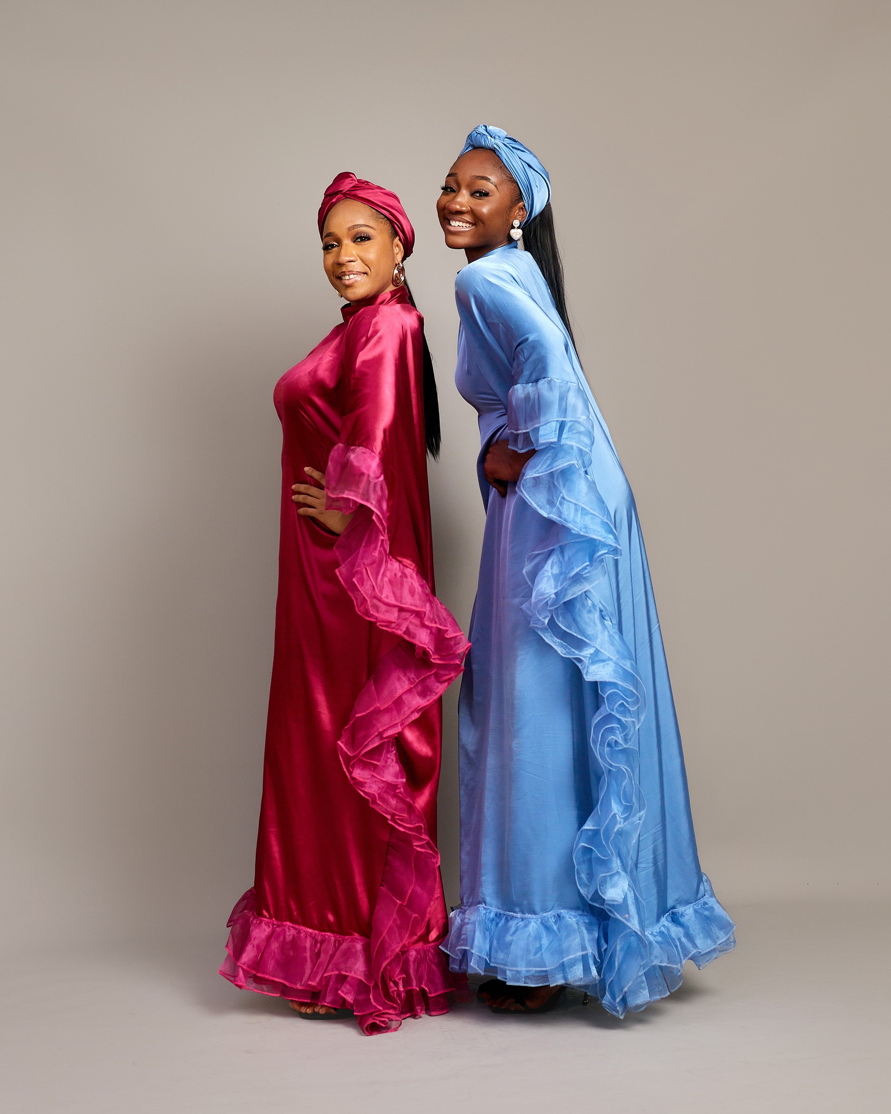 Women wearing the Ola Buubu satin gowns  with ruffle edges, long sleeves, high neckline, and matching headwraps.
