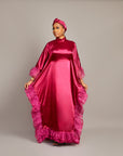 Woman wearing the Ola Buubu satin gown in pink with ruffle edges, long sleeves, high neckline, and matching headwrap.
