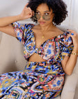 Model wearing multicolored open cut silk jumpsuit with puff sleeves and wide-leg design.
