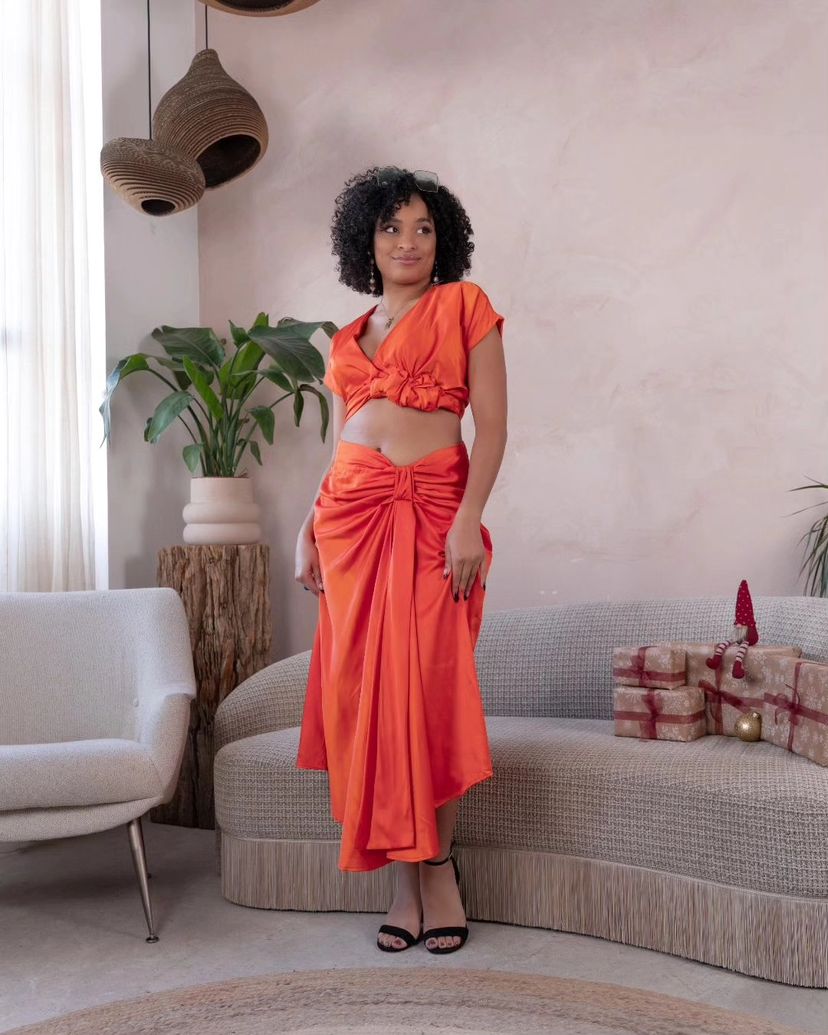  Woman wearing an orange satin crop top and matching ruched skirt, styled with statement glasses