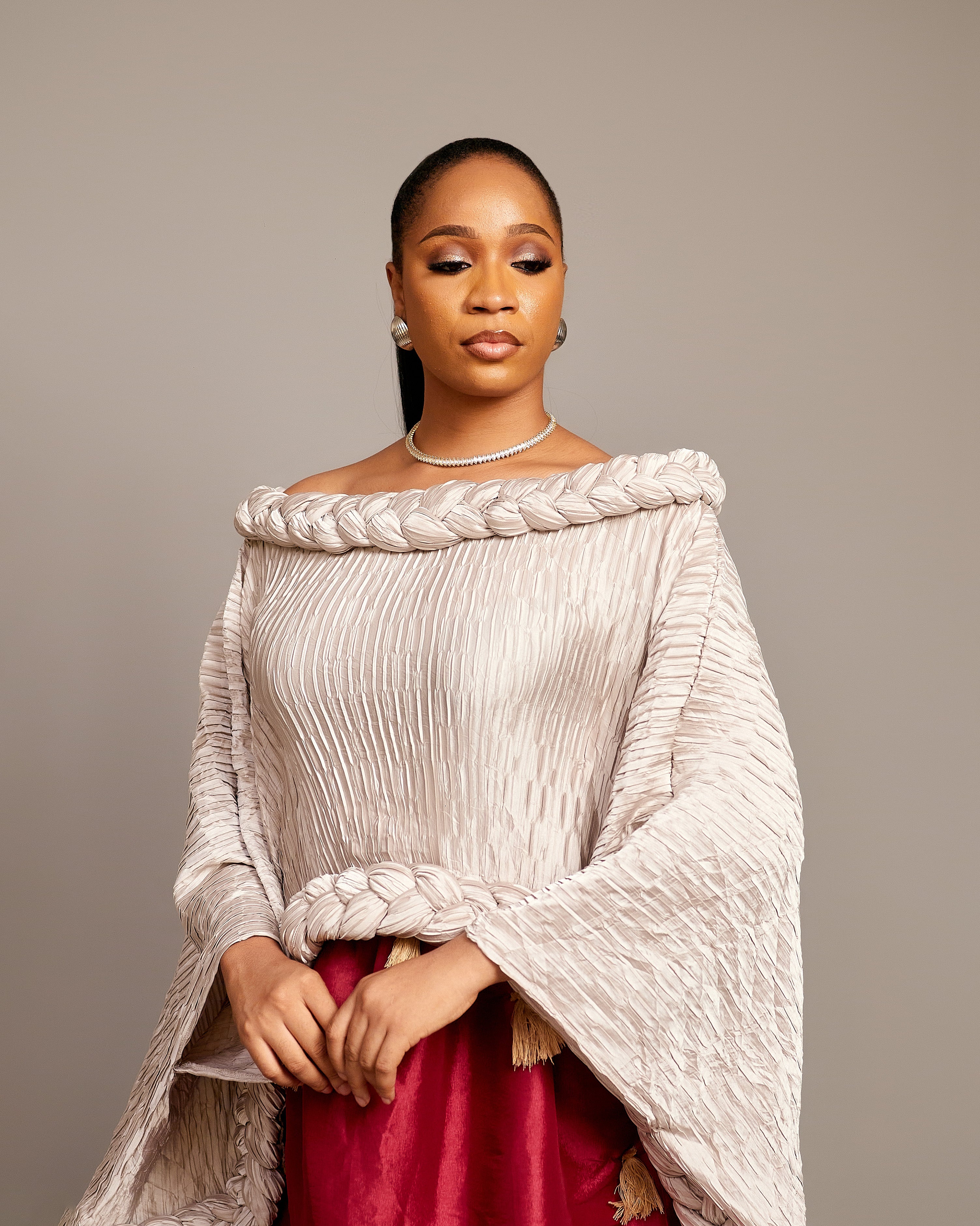 A lady wearing the Queen Ire two-piece set with textured ivory cape top and wine maxi skirt decorated with golden tassels, styled for weddings and cultural celebrations.
