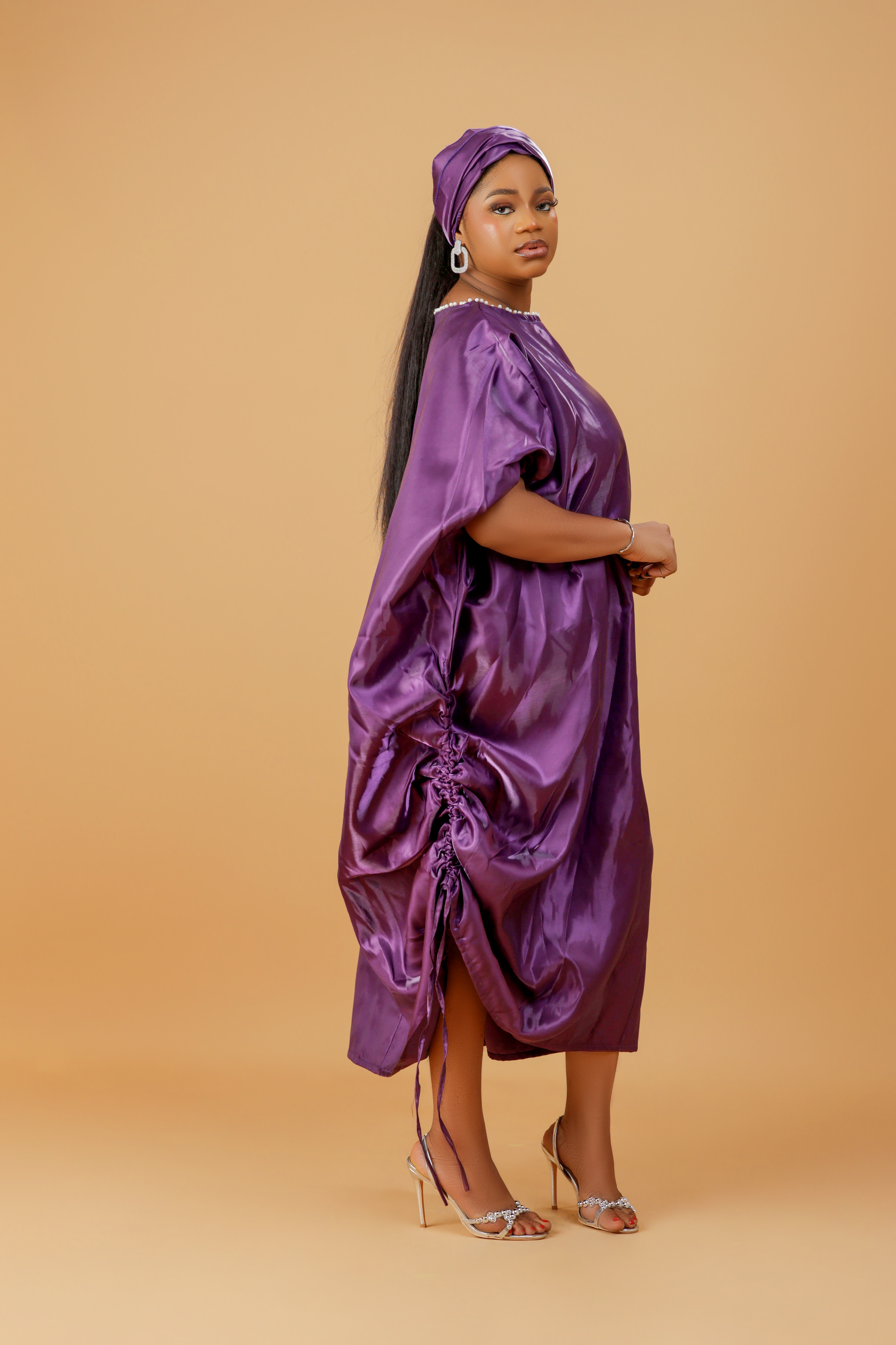 Woman wearing a regal purple satin kaftan with side drawstring detail and matching head wrap.
