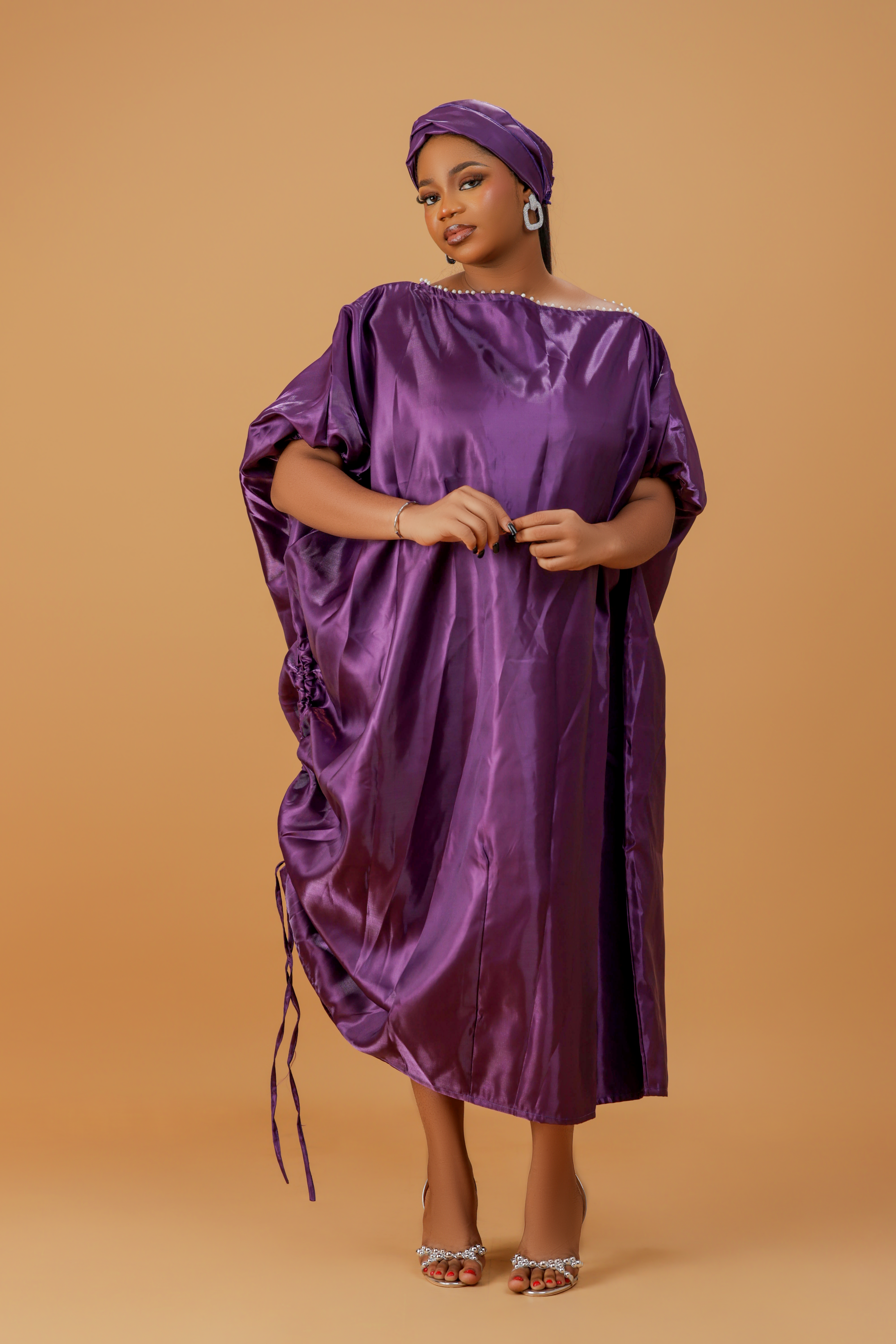 Woman wearing a regal purple satin kaftan with side drawstring detail and matching head wrap.

