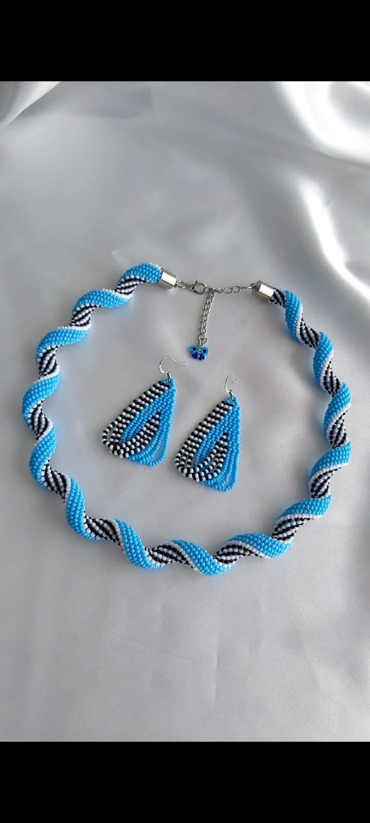 Handcrafted sapphire blue beaded jewelry set with twisted necklace and matching drop earrings on a white background.
