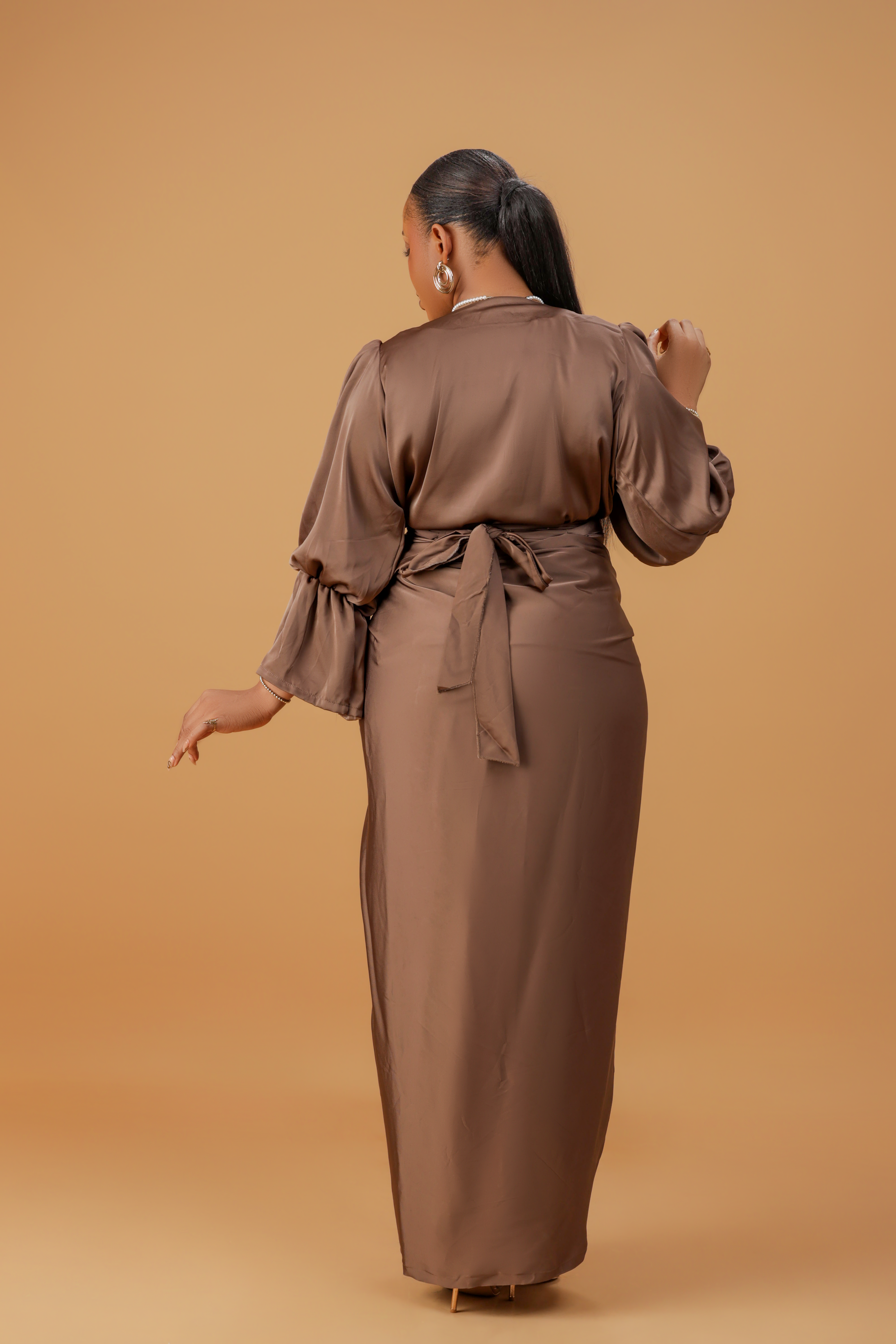 Woman wearing a coffee brown satin wrap gown with a cowl neckline and ruched waist, posing gracefully against a neutral background.
