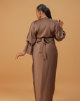 Woman wearing a coffee brown satin wrap gown with a cowl neckline and ruched waist, posing gracefully against a neutral background.
