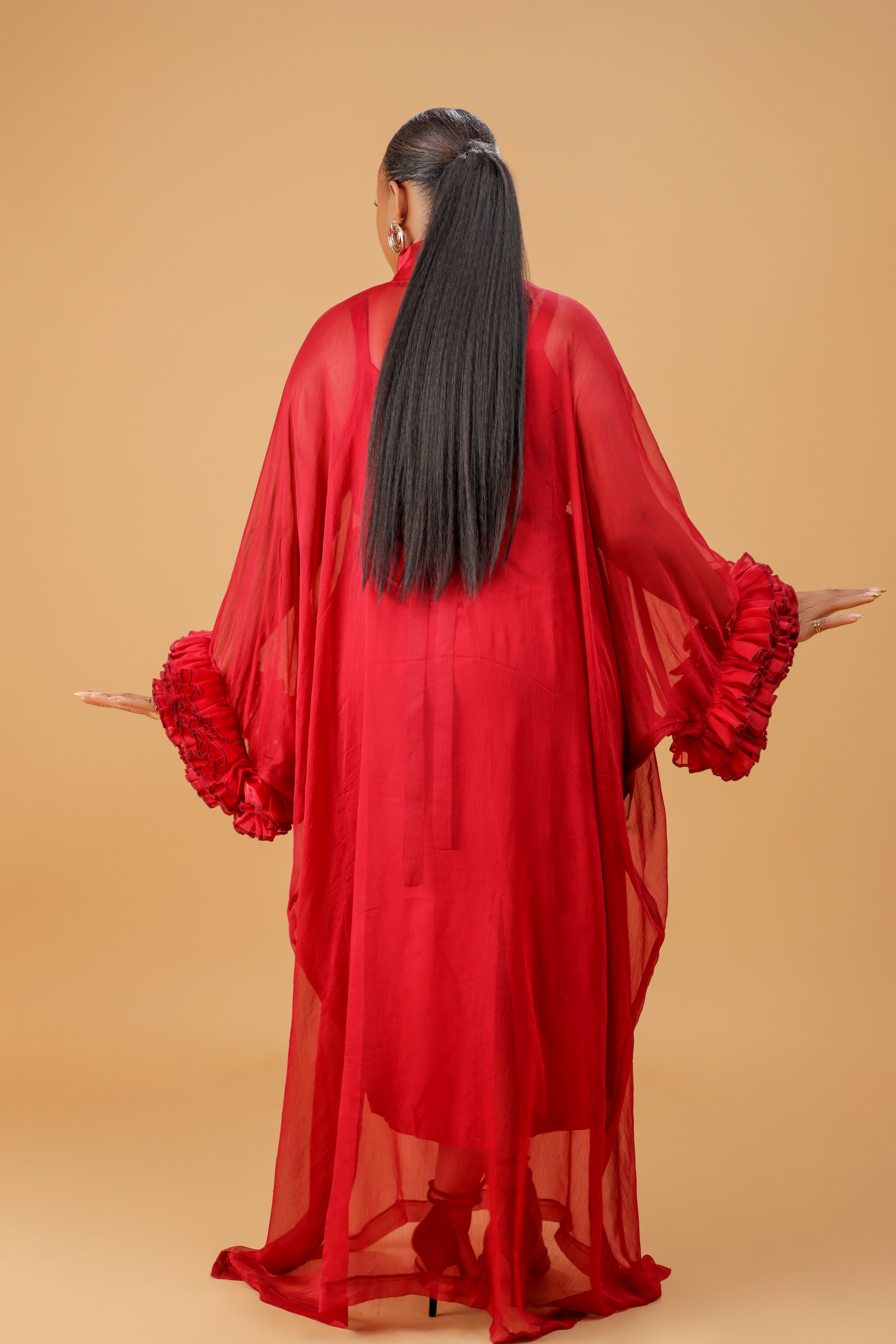 Model wearing a red organza statement dress with bow-tie neck and textured floral sleeve details, styled for formal and festive occasions.
