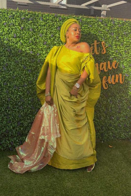 Elegant woman in a gold Show Stopper Boubou with draped detailing, posing gracefully at an outdoor event.
