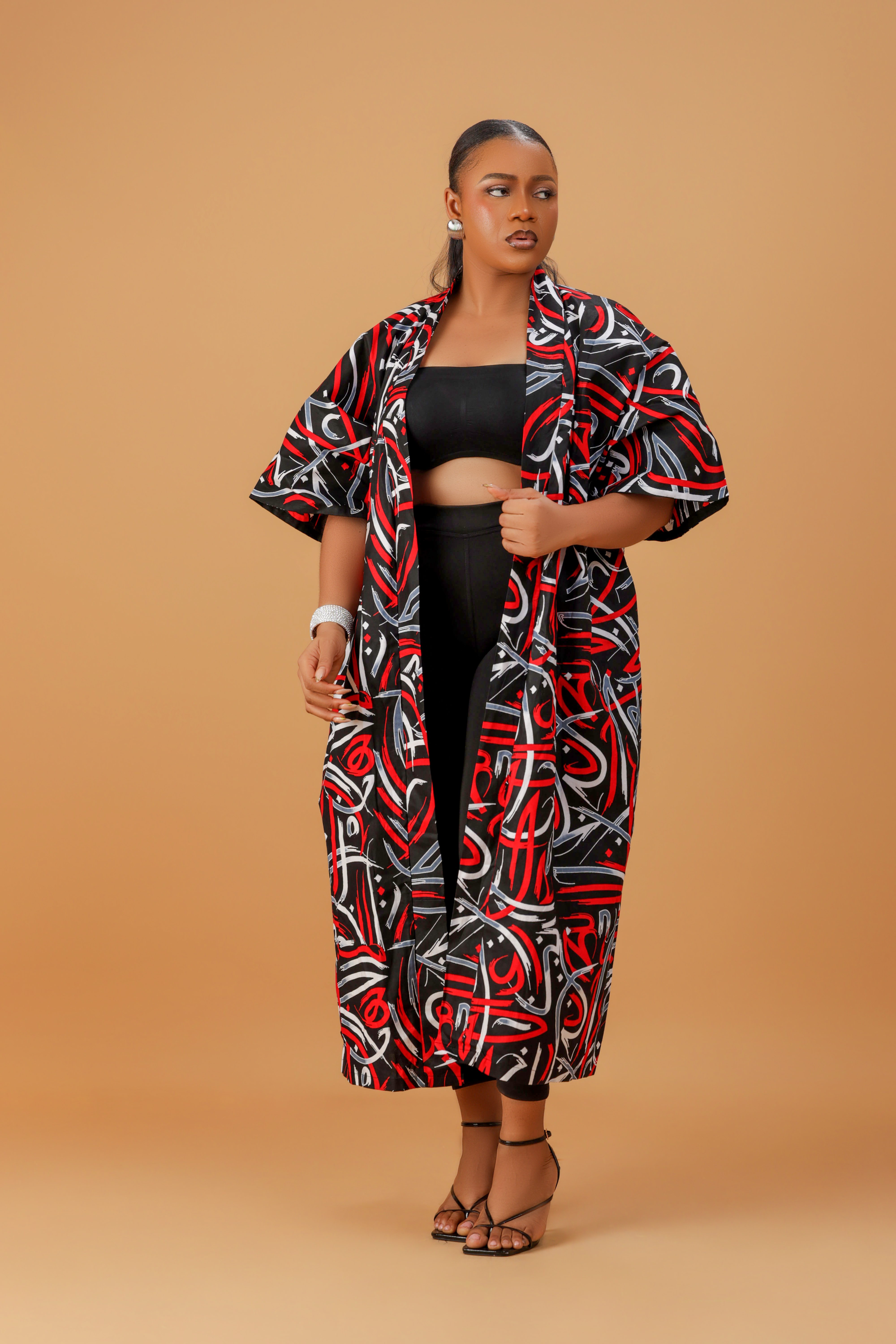 Woman wearing a bold red, black, and white abstract print kimono over a black crop top and leggings.
