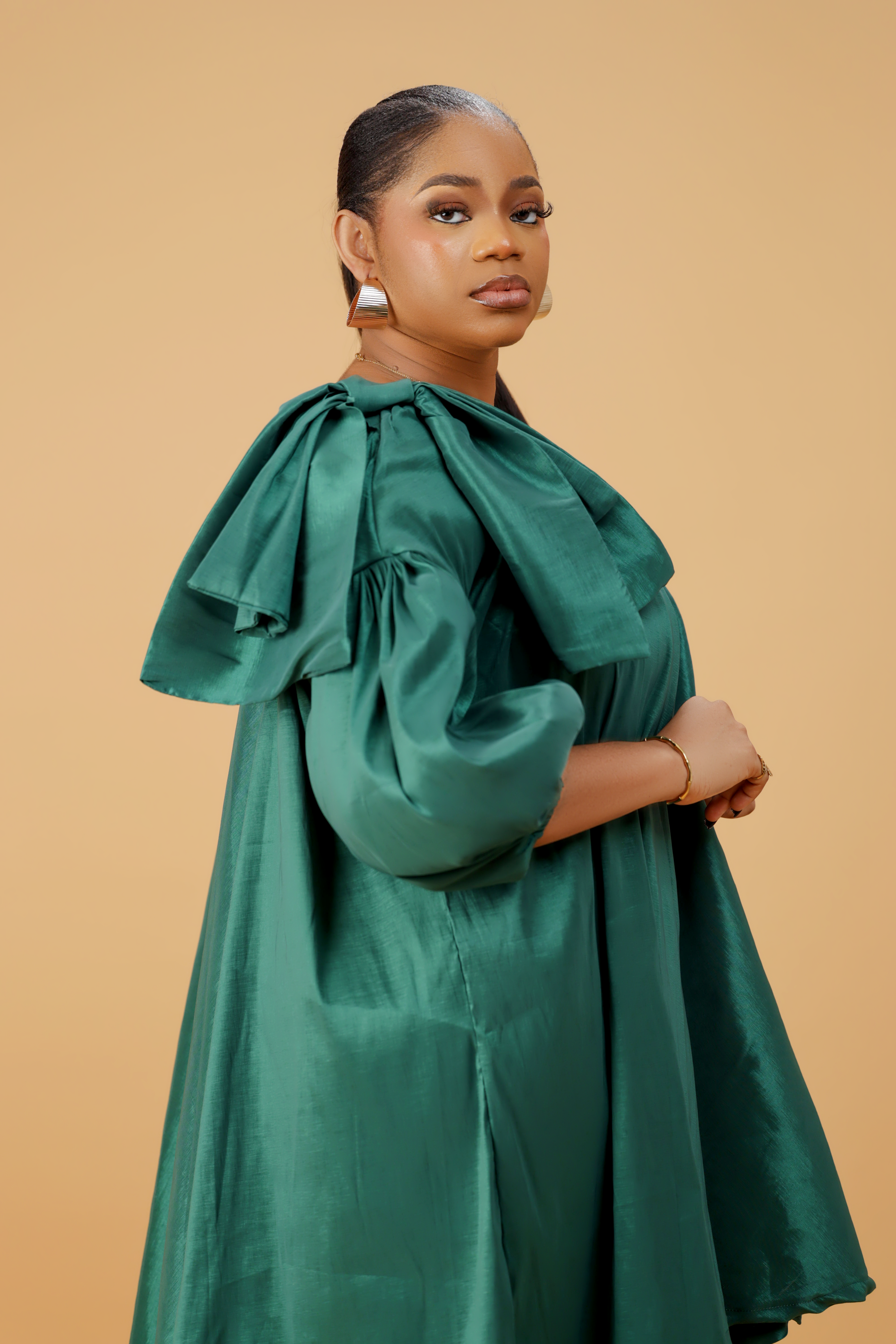 Model wearing an emerald green satin bow sleeve dress with voluminous sleeves and structured bow detail on the shoulder.
